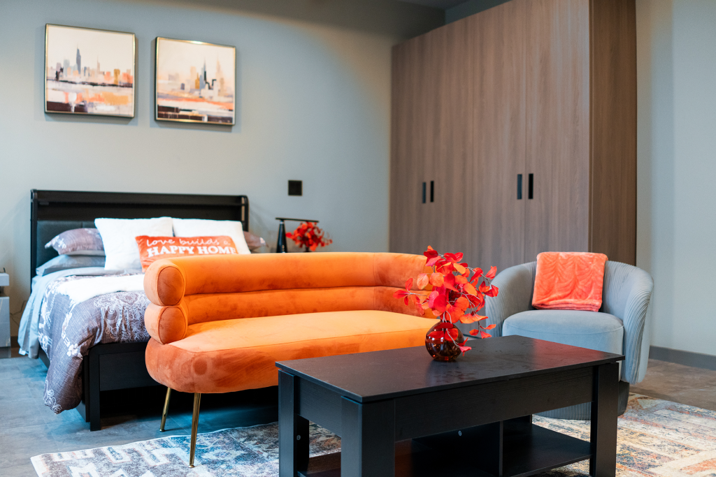 Studio apartment with an orange curved sofa, bed, wardrobe, and city skyline art on the walls